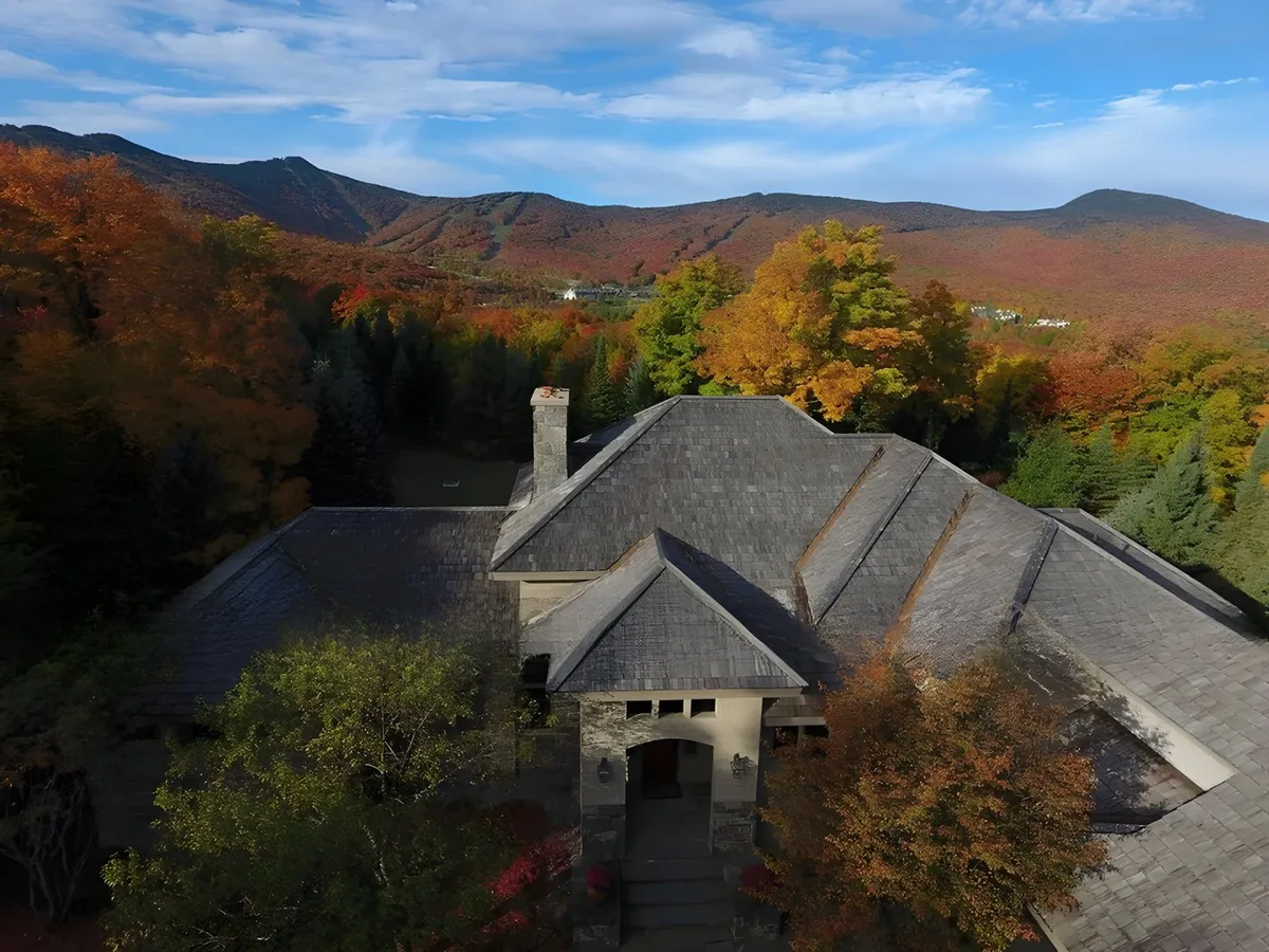 This exterior shot highlights the architectural details of the house, surrounded by vibrant autumn foliage and the sweeping Green Mountains in the background. The scene captures a tranquil and picturesque atmosphere, with the porch and yard inviting gatherings and relaxation in nature.