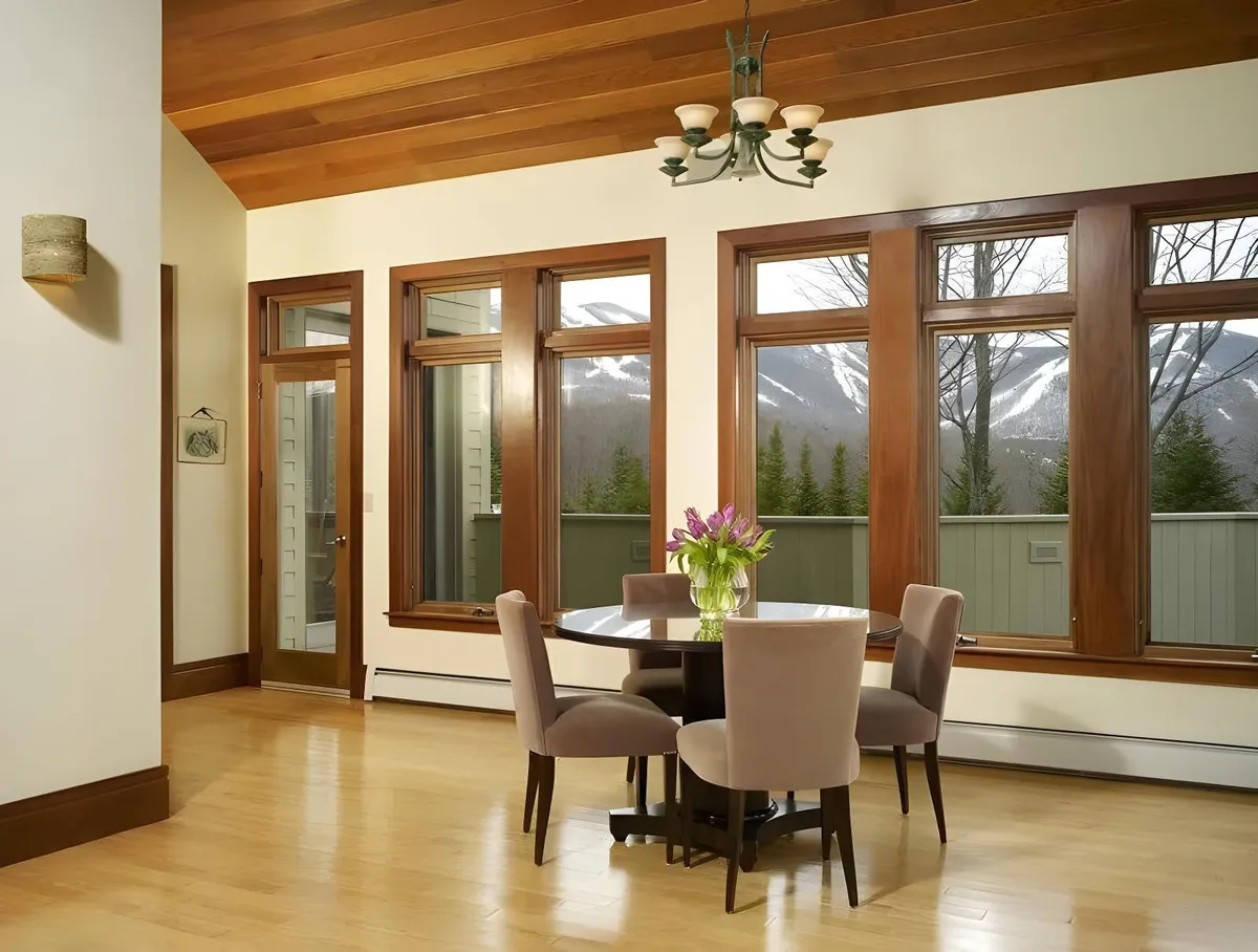 Inside, the round dining table is surrounded by chairs and set against expansive mountain views through large windows. The room emanates warmth and togetherness, hinting at shared meals, celebrations, and quiet moments enjoyed by family members of all ages.