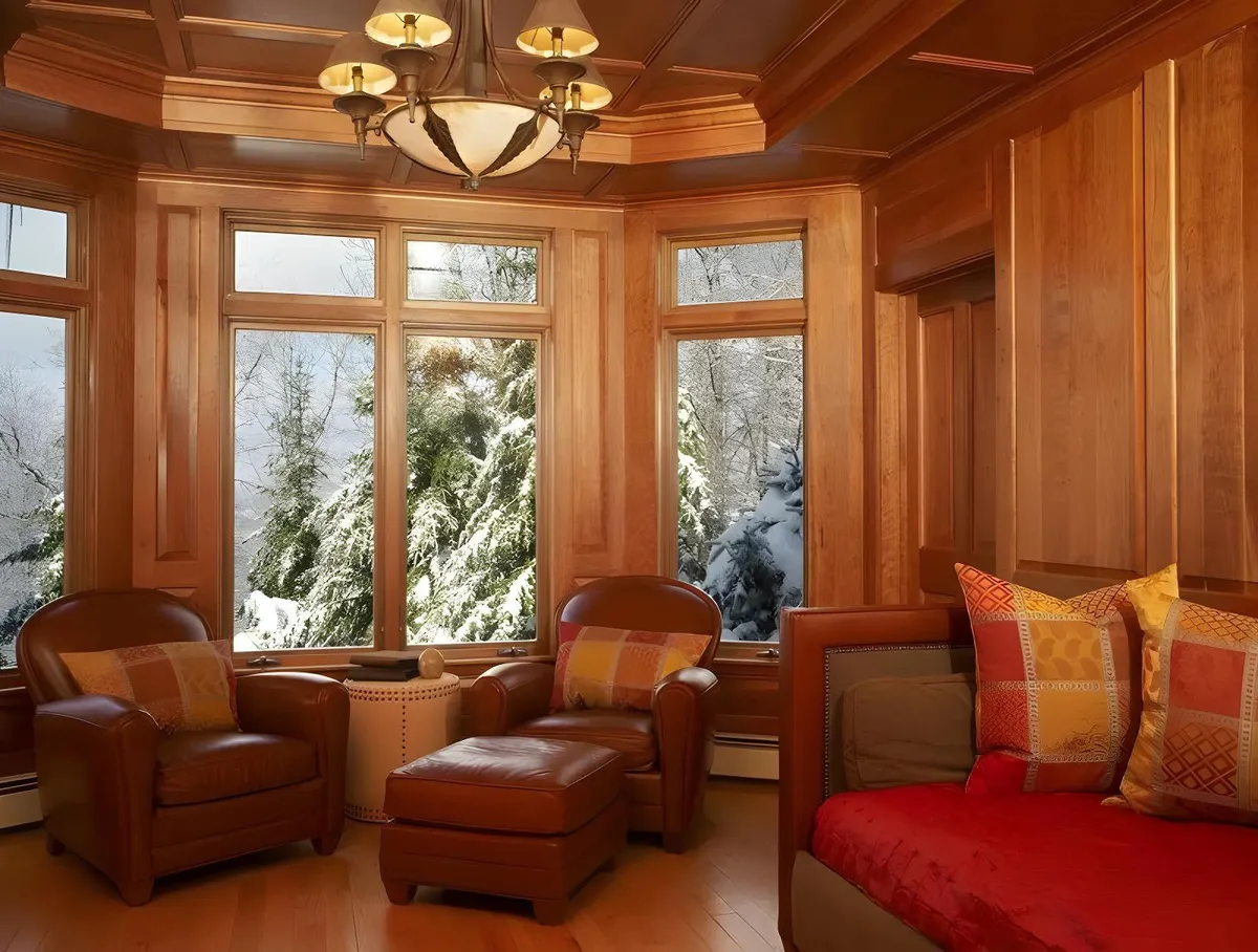 A comfortable corner with leather armchairs, large windows, wood paneling, and a chandelier. The inviting ambiance is perfect for reading, relaxing, or socializing in a cozy nook, offering versatility for both quiet and lively moments.
