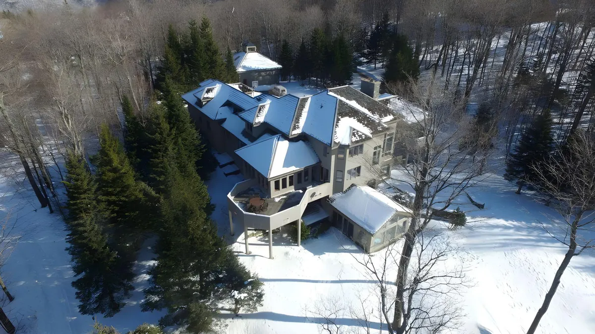 An exterior winter shot showing a large, multi-level home surrounded by snow-covered trees and expansive deck areas. The peaceful ambiance invites thoughts of ski-in/ski-out access and deck relaxation after a day outside.
