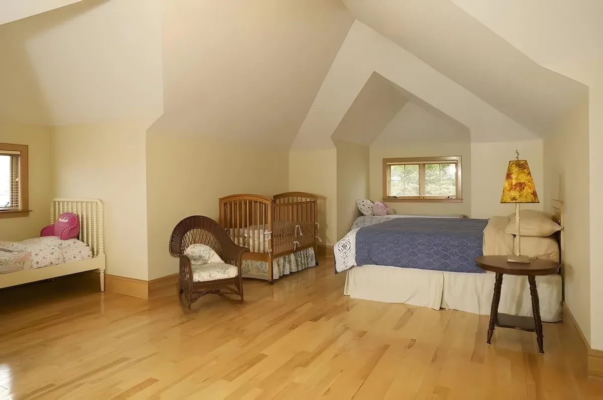 A cozy, family-friendly bedroom with a queen-sized bed, cribs, and a daybed under a softly lit lampshade. The space exudes warmth and nurturing energy, inviting both children and adults to unwind and create cherished memories together.