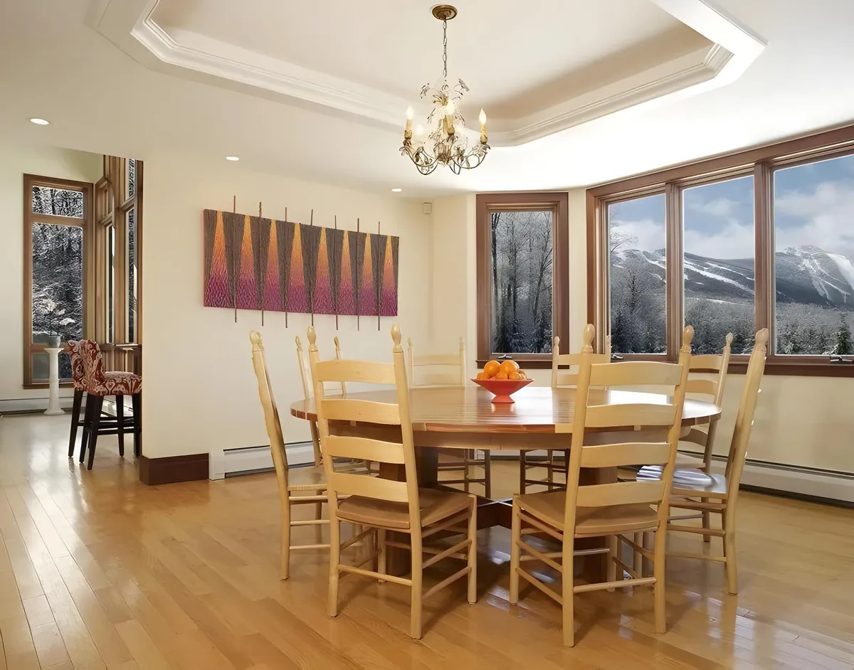 A warm and welcoming dining area highlighted by a stylish dining table under an eye-catching chandelier. Large windows frame stunning mountain vistas, while tasteful artwork on the wall and a vibrant centerpiece add a touch of regional character and sophistication.